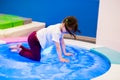 Funny girl preschooler with ponytails in a white T-shirt plays, jumps on an inflatable water trampoline with backlight.