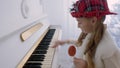 Funny girl in red hat playing music on piano and holding lollipop in hand Royalty Free Stock Photo