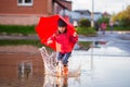 Funny girl in a red jacket and rubber boots with an umbrella jumping in the puddles Royalty Free Stock Photo