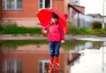 Funny girl in a red jacket and rubber boots with an umbrella stands in a puddle Royalty Free Stock Photo