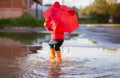 Funny girl in a red jacket and rubber boots with an umbrella walks fun through the puddles Royalty Free Stock Photo