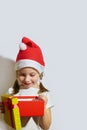 Funny girl in a Santa claus hat opens a Christmas gift, portrait of a girl on a white background Royalty Free Stock Photo