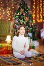 Funny girl sits on the floor next to gifts on the background of bright holiday lights