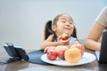 Funny girl sits table in front of phone and eats peach Royalty Free Stock Photo