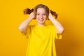 Funny girl with a two-ponytail hairstyle smiles grimaces and laughs on a yellow background