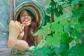 Funny girl wearing a colorful hat with lollipop and showing her feet in window with grape leaves