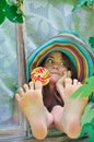 Funny girl wearing a colorful hat with lollipop and showing her feet in window with grape leaves