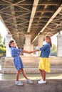 Funny girls 9 years old of different races, standing near the river under the bridge, holding hands and looking at the camera. Royalty Free Stock Photo