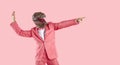 Crazy guy in party suit and dinosaur mask dancing and pointing away isolated on pink background Royalty Free Stock Photo