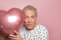 funny gray-haired elderly pensioner man holding a pink heart-shaped balloon in his hands on a pink background Royalty Free Stock Photo