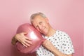 funny gray-haired elderly pensioner man holding a pink heart-shaped balloon in his hands on a pink background Royalty Free Stock Photo