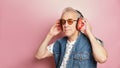funny gray-haired elderly pensioner man in sunglasses, retro headphones and denim vest with 90s style Royalty Free Stock Photo