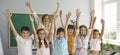 Funny group of elementary school classmates and their female teacher having fun in classroom.