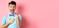 Funny guy laughing at something hilarious, smiling amazed and pointing finger at camera, standing on pink background