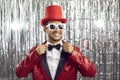 Funny guy in red sequin party suit, top hat and sunglasses smiles and fixes his bowtie Royalty Free Stock Photo