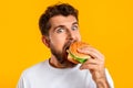 funny guy satisfying food cravings with cheeseburger on yellow background Royalty Free Stock Photo