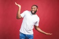 Funny guy in white t-shirt jumping and looking at camera. Studio portrait of emotional african male model posing on red background