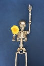 Funny Halloween concept. Golden skeletonholding yellow flower in his hands against dark gray background Royalty Free Stock Photo