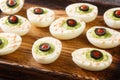 Funny Halloween food eyeballs deviled eggs stuffed with avocado cream on a wooden tray. horizontal