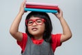 Funny and Happy Asian little preschool girl wearing red glasses holding a green book on the head, on white isolated background. Royalty Free Stock Photo