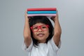 Funny and Happy Asian little preschool girl wearing red glasses holding a green book on the head, on white isolated background. Royalty Free Stock Photo