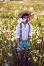 funny happy a beautiful boy child in a hat stands on a field with white dandelions at sunset in summer. soap bubbles are Royalty Free Stock Photo