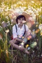 funny happy a beautiful boy child sit in hat on a field with white dandelions at sunset in summer. soap bubbles are Royalty Free Stock Photo