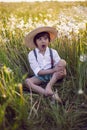 funny happy a beautiful boy child sit in hat on a field with white dandelions at sunset in summer. soap bubbles are Royalty Free Stock Photo