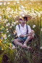 funny happy a beautiful boy child sit in hat on a field with white dandelions at sunset in summer. soap bubbles are Royalty Free Stock Photo