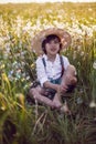 funny happy a beautiful boy child sit in hat on a field with white dandelions at sunset in summer. soap bubbles are Royalty Free Stock Photo