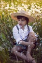 funny happy a beautiful boy child sit in hat on a field with white dandelions at sunset in summer. soap bubbles are Royalty Free Stock Photo