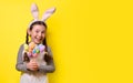 Funny happy girl with Easter bunny ears is holding colorful Easter eggs on a yellow background. Happy Easter! Copy space. Banner Royalty Free Stock Photo