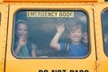 Funny happy smiling boy and girl kids students looking out of school yellow bus window. Waving saying goodbye to parents before