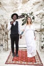Funny hippy Wedding couple dressed in boho style are staying before the wedding arch in canyon outdoors. boho wedding