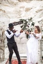 Funny hippy Wedding couple dressed in boho style are staying before the wedding arch in canyon outdoors and showing