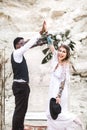 Funny hippy Wedding couple dressed in boho style are staying before the wedding arch in canyon outdoors and smiling