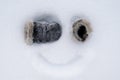 Funny homemade smiley face, with mittens instead of eyes and a painted smile on the snow. Creative idea. Top view.