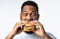 Funny Hungry African Guy Eating Burger Standing On White Background