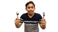Funny and hungry face expression of young Asian Malay man with strips t-shirt holding a spoon and fork ready to eat