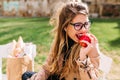 Funny hungry girl with appetite bites off red apple sitting in the park after a shopping trip. Attractive young woman