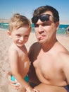 Funny image of young man with his little son showing tongues in camera while making selfie photo at sea beach. Family Royalty Free Stock Photo