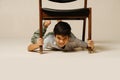 Funny indian boy playing with an armchair lying under it, holding by the legs Royalty Free Stock Photo