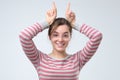 Funny joking young woman making horns with fingers