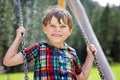 Funny kid boy having fun with chain swing on outdoor playground while being wet splashed with water. child swinging on Royalty Free Stock Photo