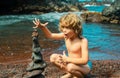 Funny kid boy making stack of pebbles stone against sea background for spa, balance, meditation and zen theme. Child Royalty Free Stock Photo