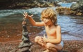 Funny kid boy making stack of pebbles stone against sea background for spa, balance, meditation and zen theme. Child Royalty Free Stock Photo