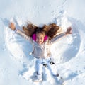 Funny kid making snow angel. Child girl playing and making a snow angel in the snow. Top view. Royalty Free Stock Photo