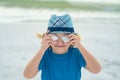 Funny kid playing outdoor on summer beach. Child picked up the seashell and closed his eye. Little girl playing on the Royalty Free Stock Photo