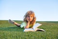 Funny kid reading the book in spring park. Child boy is reading a book on the spring park. Relaxing on the grass in the Royalty Free Stock Photo