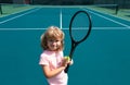 Funny kid tennis player on tennis court. Child boy with tennis racket and tennis balls.